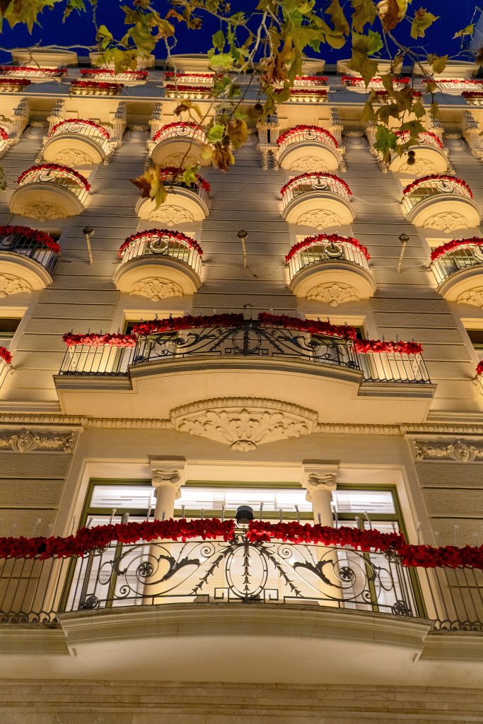 un immeuble du quartier Eixample pris par une vue basse, il y a des fleurs rouges aux balcons